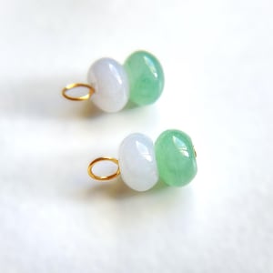 May include: Two pairs of jade earrings. Each earring features a white and a green jade bead, connected by a gold-colored loop. The earrings are set against a white background, highlighting the natural colors and textures of the jade.