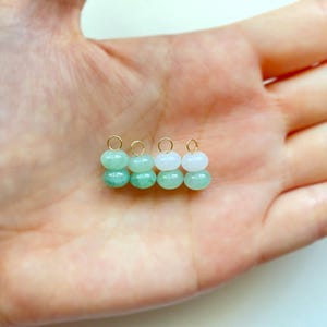 May include: Four small, beaded earrings with gold-colored hoops. The earrings are made of two stacked, round beads. The beads alternate between light green and white. The earrings are displayed on a light-colored background.