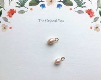 May include: Two small, off-white pearl charms with gold jump rings. The charms are on a white background with the text "The Crystal You" printed in black.