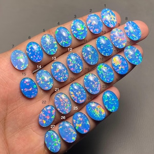 May include: Twenty-seven oval-shaped blue opals with iridescent rainbow flashes. The opals are numbered 1 through 27.