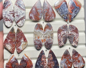 May include: Set of 9 pairs of agate cabochons, each pair is numbered 1 through 9. The cabochons are various shapes and sizes, with a mix of red, white, and gray colors.