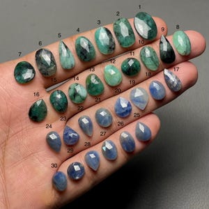 May include: A selection of gemstones, including emeralds and sapphires, in diverse shapes and cuts. The emeralds vary in shade from light to dark green, while the sapphires are a deep blue. The gemstones are numbered 1 to 30.