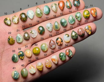 May include: Forty-one polished gemstone cabochons in diverse colours and patterns, including green, red, orange, and white. Each stone is numbered and displayed on a hand, showcasing their unique shapes and textures. Suitable for jewellery making or collecting.