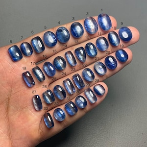 May include: A selection of 33 blue kyanite gemstones in diverse forms. The gemstones, numbered 1 to 33, are oval, rectangular, and teardrop-shaped, exhibiting a translucent appearance. The stones are of varying sizes.