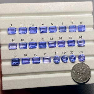 May include: A white display tray with 24 rectangular and round blue gemstones arranged in rows. The gemstones are labeled with numbers 1 through 24. A Malaysian 20 ringgit coin is in the lower right corner of the image.