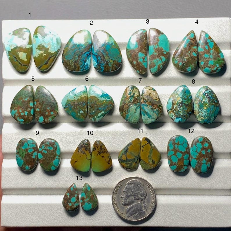 May include: A collection of turquoise gemstones in various shapes, including oval and teardrop. The stones display a mix of blue, green, and brown hues, with unique veining patterns. A US nickel coin is included for size reference.