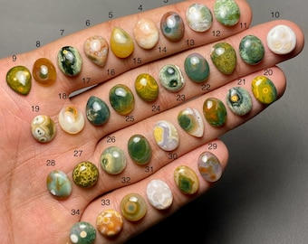 May include: A selection of 34 polished gemstone cabochons in diverse shapes and colours, including green, yellow, orange, and white. Each stone is numbered, displaying the variety of natural stone patterns and hues.