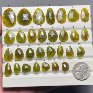 以下が含まれることがあります： 黒い持ち手と「But First, Coffee」のテキストが黒い太字で書かれた白いセラミックマグ。マグは白い表面に置かれています。マグの高さは約10cmです。