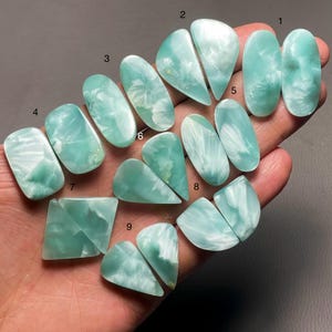 Pode incluir: Nove cabochões de pedra preciosa verde e branca iridescente de várias formas e tamanhos, numerados de 1 a 9.