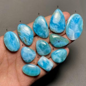 Op de afbeelding: Elf blauwe en witte cabochon edelstenen met een draaiende structuur. De edelstenen zijn genummerd van 1 tot en met 11.