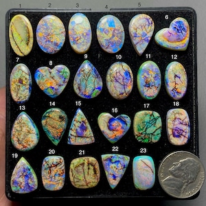 May include: A collection of polished opal gemstones in various shapes, including oval, teardrop, heart, and triangular forms. The opals display vibrant colors with internal patterns, set against a black background. A US nickel coin is included for size reference.