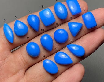Puede incluir: Una colección de catorce gemas pulidas de color azul vibrante en varias formas, incluyendo ovaladas, en forma de lágrima y rectangulares. Las gemas se muestran sobre un fondo neutro, mostrando su color brillante y superficies lisas. Ideales para la creación de joyas.