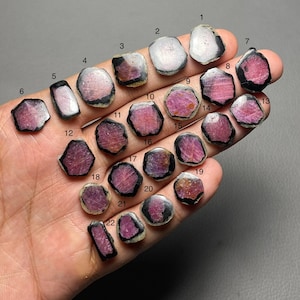 Puede incluir: Una colección de 22 piedras preciosas en bruto, cada una con una forma y color únicos. Las gemas presentan una mezcla de tonos rosas, morados y claros, con bordes oscuros. Las piedras preciosas están numeradas del 1 al 22.