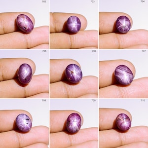 May include: Nine oval-shaped, polished gemstones in shades of purple. Each gem has a star-like effect across its surface. The gems are displayed on a light background, held by a hand.