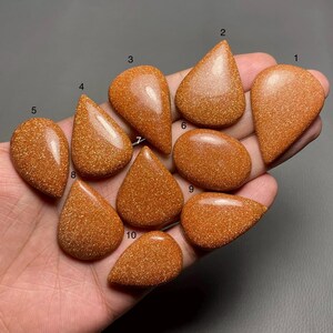 May include: Ten teardrop-shaped cabochons of golden sandstone, each with a unique sparkle and texture. The stones are numbered 1 through 10.