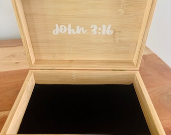 Puede incluir: Una caja de madera con un interior de terciopelo negro y un cierre de latón. La tapa de la caja tiene las palabras "Juan 3:16" grabadas.
