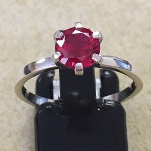 May include: A silver ring with a red ruby gemstone set in a prong setting.
