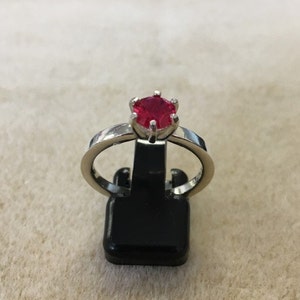 May include: A silver ring with a red gemstone set in a prong setting.
