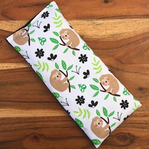 May include: White eye pillow with a black and green sloth pattern. The pillow is filled with flax seeds and lavender.