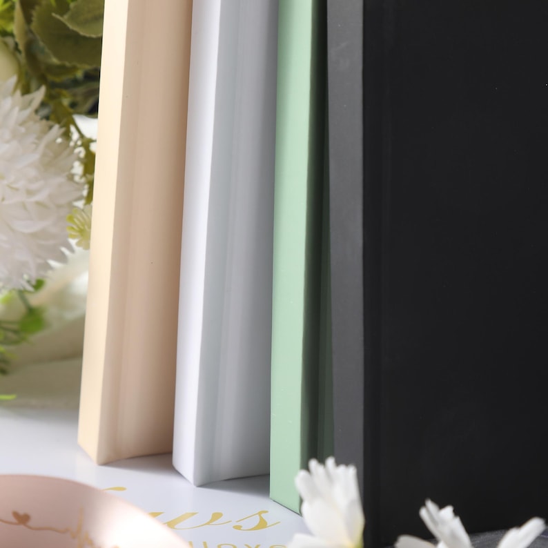 May include: A set of four rectangular frames standing upright in a row, featuring a smooth matte finish in shades of cream, white, light green, and black. Each frame has a clean, flat edge profile and a solid, uniform color throughout the surface.