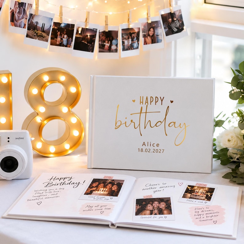 May include: A white photo album with gold foil text reading Happy birthday Alice 18.02.2027. The open album displays handwritten notes and square photographs. A gold light-up number 18 and a white instant camera are positioned next to the album.