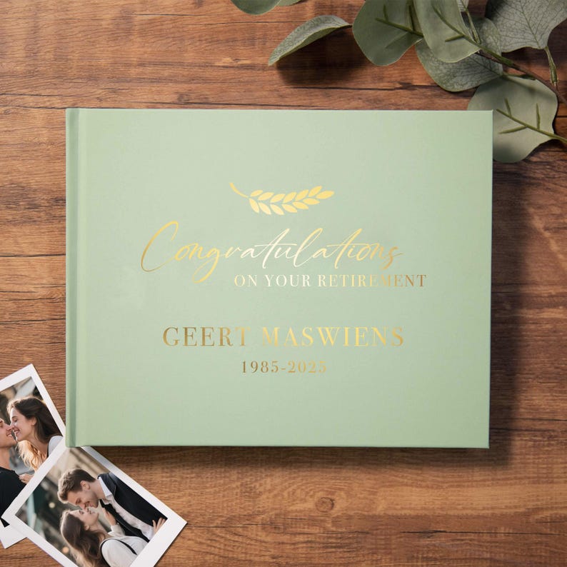 May include: A light green hardcover book with gold foil text that reads Congratulations ON YOUR RETIREMENT, GEERT MASWIENS, and 1985-2023, featuring a gold leaf graphic above the text. The book is positioned next to two small photographs.