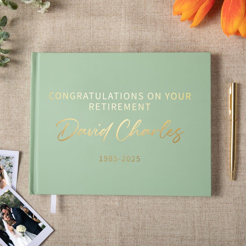May include: A sage green hardcover guest book featuring gold foil text that reads CONGRATULATIONS ON YOUR RETIREMENT, David Charles, and 1985-2025. The book is positioned next to a gold pen, with a small photograph of a couple visible nearby.