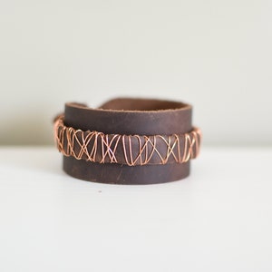 May include: A brown leather cuff bracelet with a copper wire design.