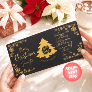 May include: A rectangular black gift card with gold foil text and snowflake accents. The card features the text Merry Christmas Samantha, a gold Christmas tree with a scratch-off area labeled SPA DAY, and a holiday message signed Love, Tom.