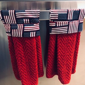 May include: Two red kitchen towels with a patriotic American flag design. The towels are hanging on a silver towel rack.