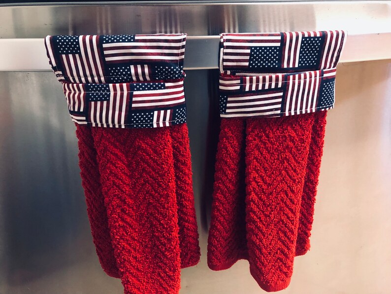 May include: Two red kitchen towels with a patriotic American flag design. The towels are hanging on a silver towel rack.