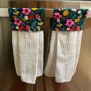 May include: Two white kitchen towels with green, pink, yellow, and red floral print fabric hanging on a silver towel rack.