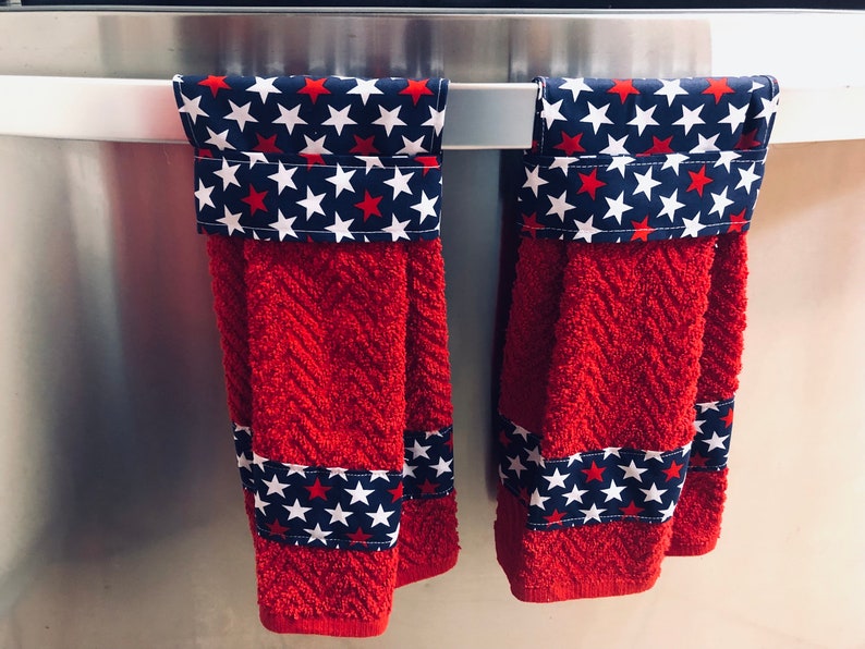 May include: Two red kitchen towels with white stars on a blue background. The towels are hanging on a silver rack.