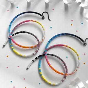 May include: Two pairs of rainbow beaded hoop earrings. The earrings are made with small colourful beads and have a wire hoop design. (rainbow)
