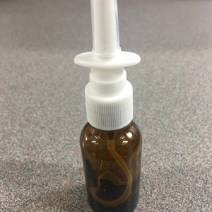May include: A brown glass bottle with a white spray nozzle and a white cap. The bottle is about 4 inches tall.