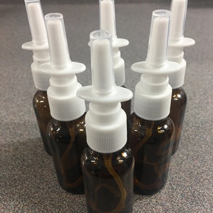 May include: Six amber glass bottles with white spray tops. The bottles are filled with a clear liquid.