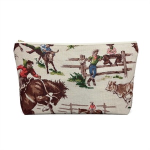 Puede incluir: Una bolsa blanca con cremallera con un patr&oacute;n repetido de vaqueros montando caballos y toros. Los vaqueros llevan ropa y sombreros coloridos. El fondo es beige claro con una valla marr&oacute;n y hierba verde.