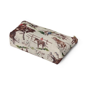 Puede incluir: Una bolsa de cremallera beige con un patr&oacute;n repetido de vaqueros montando a caballo y ganado. El patr&oacute;n est&aacute; en tonos de marr&oacute;n, rojo, azul y verde.