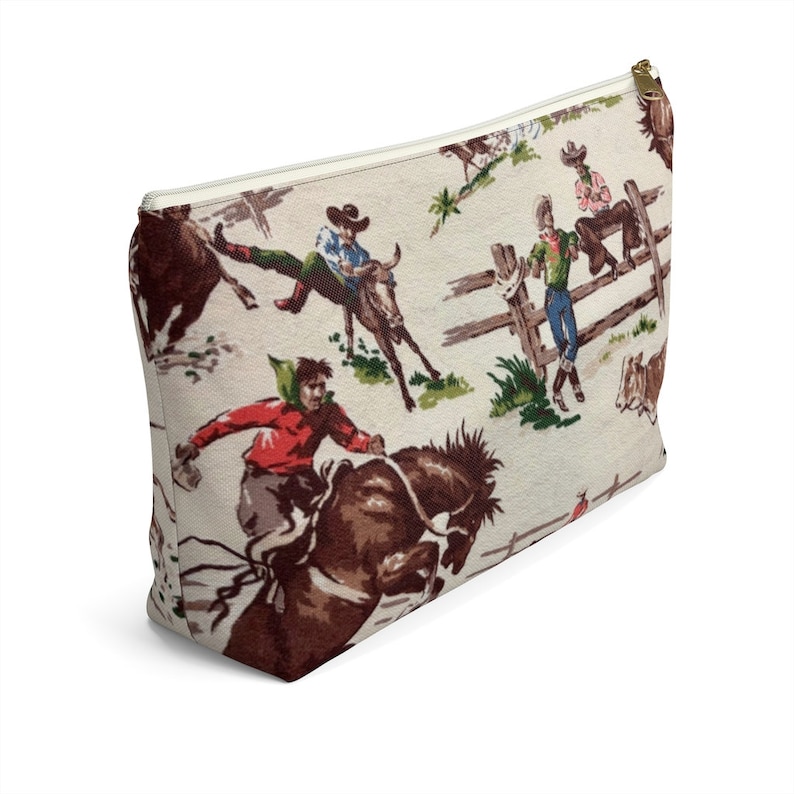 Puede incluir: Una bolsa blanca con cremallera con un patr&oacute;n vintage de vaqueros montando caballos y toros. El patr&oacute;n est&aacute; en tonos de marr&oacute;n, rojo, verde y azul.