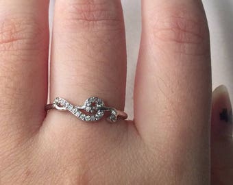 May include: A silver ring with a delicate design featuring a small cluster of clear stones. The ring is worn on the ring finger of a hand.