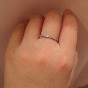May include: A silver band ring with small, clear gemstones set in a delicate, scalloped design.