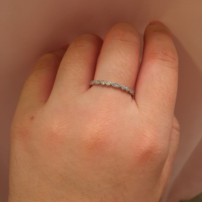 May include: A silver band ring with small, clear gemstones set in a delicate, scalloped design.