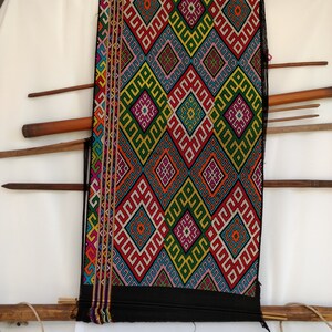May include: A black fabric with a colourful geometric pattern woven into it. The fabric is stretched on a wooden frame.