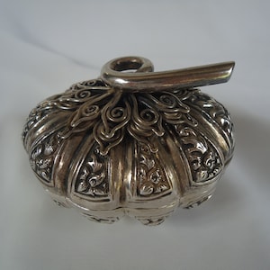 May include: A silver, ornate, decorative box with a hinged lid and a detailed, scroll-like handle.