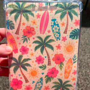 May include: A clear protective tablet case featuring a repeating summer pattern on a light background. The design includes green palm trees, vibrant pink and orange hibiscus flowers, yellow suns, and colorful surfboards in shades of pink and blue.