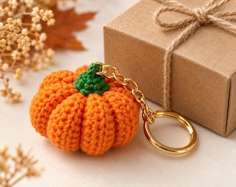 May include: A crocheted orange pumpkin keychain with a green stem, attached to a gold-toned metal chain and a circular split ring. The pumpkin features a ribbed texture created by yarn stitches, providing a soft, rounded appearance for the accessory.