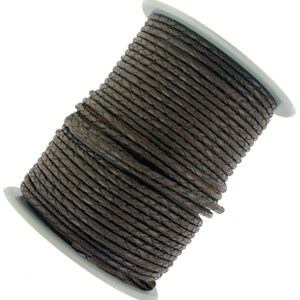 May include: A spool of brown leather cord, wound tightly in a spiral shape. The cord is textured and has a braided appearance.