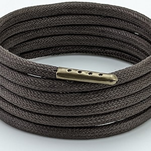 May include: A brown braided rope bracelet with a gold metal clasp. The clasp has five holes and a pointed end.