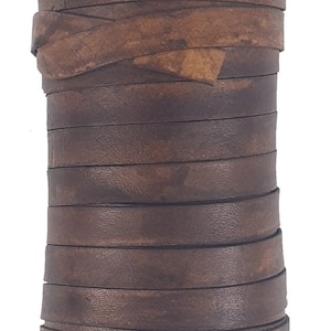 May include: A roll of dark brown leather strips, ideal for crafting. The leather has a textured surface and a rich, aged appearance. The roll sits on a black base. The leather strips are approximately 1.27 cm wide.