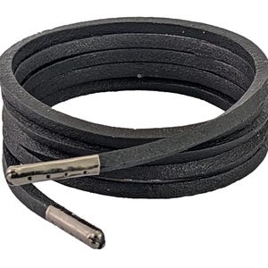 May include: Black leather cord with silver metal tips. The cord is wrapped around itself in a circle.